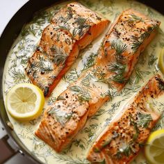 three salmon fillets in a skillet with lemons and rosemary garnish