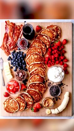 pancakes, strawberries, bananas, blueberries and other foods are arranged on a cutting board