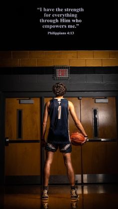 a man holding a basketball standing in front of a door with a quote on it