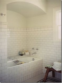 a white tiled bathroom with a bathtub and sink in it's corner, next to a window