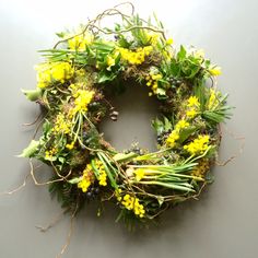 a wreath with yellow flowers and greenery hanging from the side on a gray wall