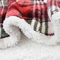 a plaid blanket is laying on top of a white bed sheet with red and green flannel