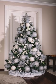 a silver and white christmas tree with ornaments on it's base in front of a door