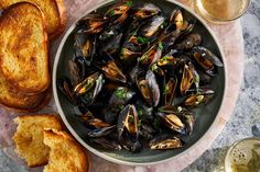 a bowl of mussels next to some toasted bread and a glass of beer