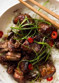 a white bowl filled with rice and meat next to chopsticks on top of it