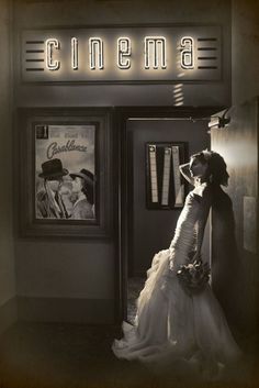 a black and white photo of a woman standing in front of a movie theater