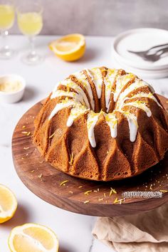 a bundt cake with icing and lemons on a wooden platter next to plates