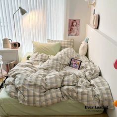 an unmade bed with plaid sheets and pillows in a bedroom next to a window