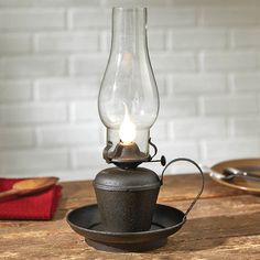 an old fashioned oil lamp on a saucer sits on a wooden table with plates and utensils in the background