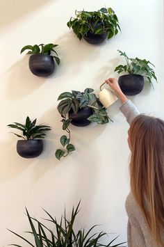 a woman is reaching up to plants on the wall