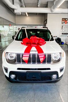 a white jeep with a red bow on it's hood in a showroom