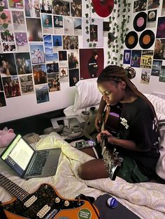 a woman sitting on a bed with a laptop and guitar in front of her,