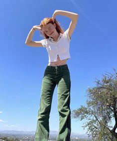 a woman standing on top of a rock with her hands behind her head and looking at the camera