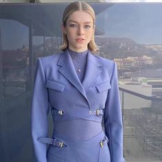 a woman in a blue suit standing on top of a building next to a window