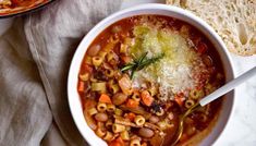 a bowl of pasta soup with bread on the side