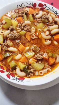 a white bowl filled with pasta and meat soup on top of a red table cloth