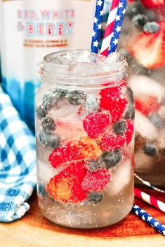 two mason jars filled with ice and strawberries on top of a wooden table next to an american flag napkin