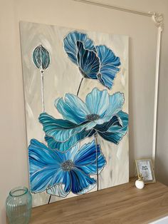 a painting with blue flowers on it sitting on a shelf next to a vase and lamp