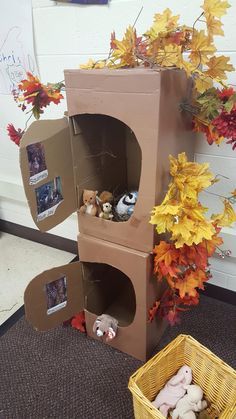 there is a cardboard box with stuffed animals in it on the floor next to fall leaves