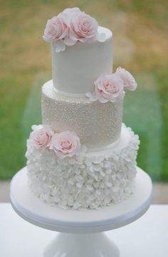 a three tiered wedding cake with pink flowers on top is sitting on a white pedestal