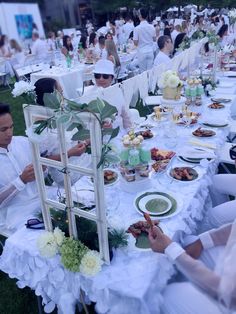 a group of people sitting around a table with plates and bowls on it, all dressed in white