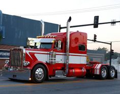 a red and white semi truck driving down a street next to a traffic light on a pole