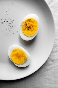 two hard boiled eggs on a white plate with black pepper sprinkles and seasoning