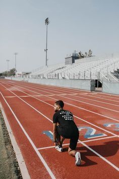 a man kneeling down on a track in front of an empty stadium