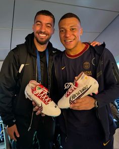 two men standing next to each other holding sneakers