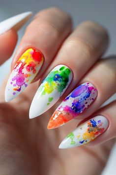 Close-up of a hand with long, pointed nails featuring a colorful splatter paint design.