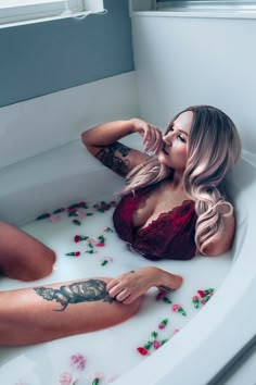 a woman sitting in a bathtub with rose petals on the floor and her legs