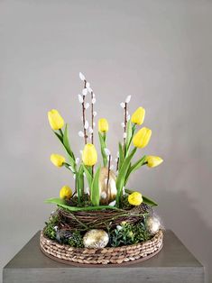 a basket filled with yellow and white flowers on top of a wooden table next to a gray wall