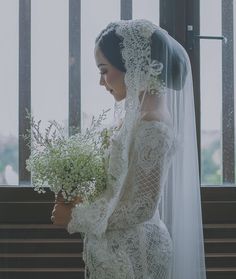 a woman in a wedding dress holding a bouquet of flowers and looking out the window