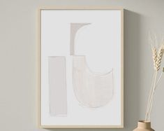 a white vase sitting on top of a wooden table next to a framed art piece