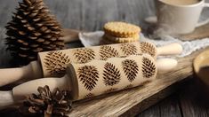 three wooden rolling pins with pine cones and cookies in the background on a table next to two mugs