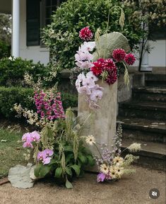 an arrangement of flowers sitting on the ground in front of a house