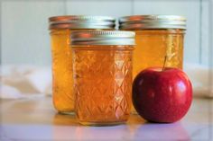 three jars filled with apple jam sitting on top of a white counter next to an apple