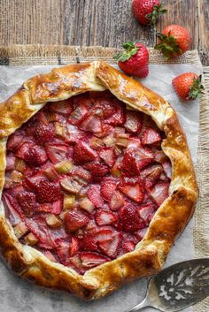 a pie with strawberries on top and spoons next to it