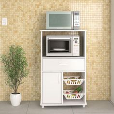 a microwave oven sitting on top of a white cabinet next to a potted plant