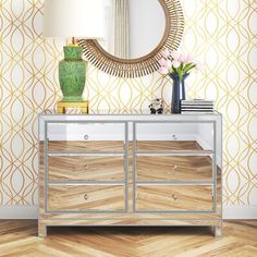 a white dresser sitting next to a green vase on top of a wooden floor in front of a mirror