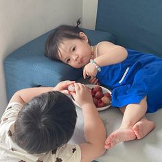 two children are sitting on the couch eating strawberries from a plate and looking at each other