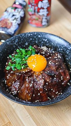 a black bowl filled with meat and an egg on top of sesame seed sprinkled rice