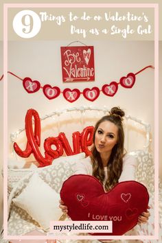 a woman holding a heart shaped pillow with the words love on it in front of her