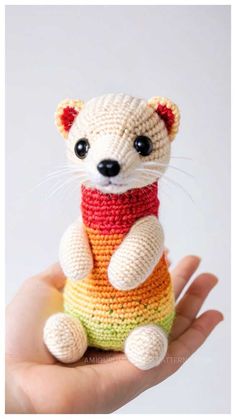 a hand holding a small crocheted animal in a rainbow colored sweater with black eyes