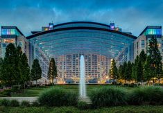 a large building with a fountain in front of it at night, surrounded by trees and grass