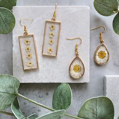 three different types of earrings sitting on top of a white marble slab next to green leaves