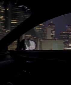 the view from inside a car at night with skyscrapers in the background and buildings lit up