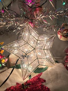 a star shaped ornament hanging from a christmas tree with other ornaments around it