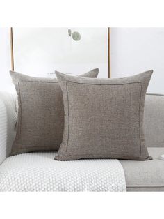 two pillows sitting on top of a couch in front of a white pillow and blanket