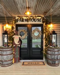 the front door of a farm house decorated with wreaths, lights and two wine barrels